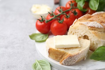 Slices of baguette with butter, basil and tomatoes on light grey table, closeup. Space for text