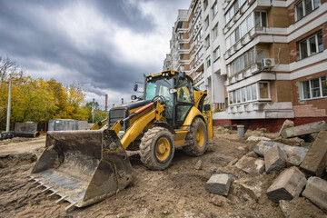 Construction equipment works on a building site with cloudy skies and autumn trees in the background