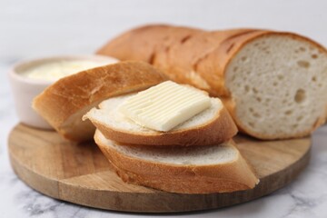 Cut baguette with butter on white marble table, closeup