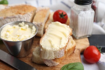 Cut baguette with butter, basil, tomatoes and knife on light table, closeup