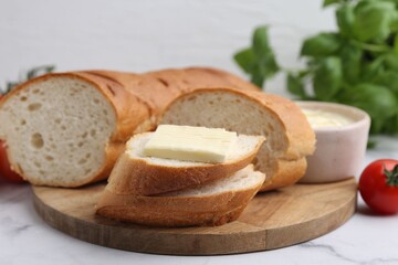 Cut baguette with butter, basil and tomato on white marble table, closeup