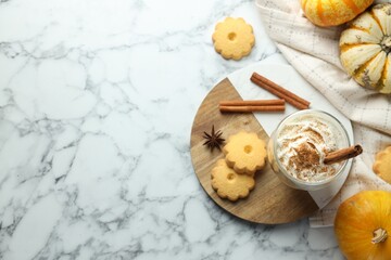 Tasty pumpkin latte with whipped cream in glass, cookies and ingredients on white marble table, flat lay. Space for text