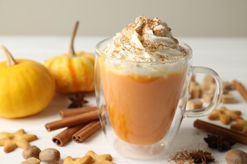 Tasty pumpkin latte with whipped cream in glass cup, cookies and ingredients on white wooden table, closeup