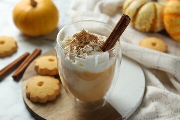 Tasty pumpkin latte with whipped cream in glass, cookies and ingredients on white marble table, closeup