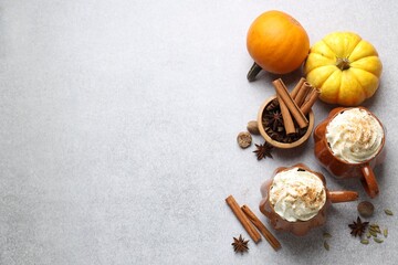 Fototapeta premium Tasty pumpkin latte with whipped cream in cups, spices and ingredients on light grey table, flat lay. Space for text