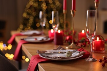Stylish Christmas table setting with plates, glasses and burning candles in festive decorated room,...