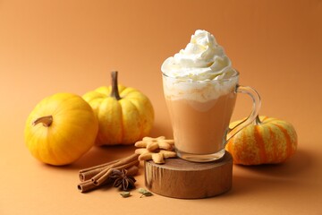 Tasty pumpkin latte with whipped cream, spices, cookies and fresh vegetables on orange background