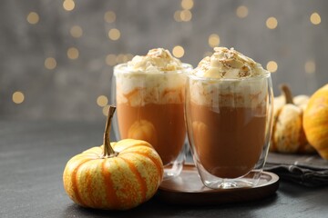 Tasty pumpkin latte with whipped cream and fresh vegetables on black table against blurred lights, closeup