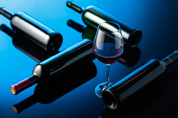 Glass and bottles of red wine on a black reflective background.