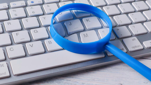 Bright Blue Magnifying Glass Resting on a Modern Wireless Keyboard for Online Search and Digital Investigation - Powered by Adobe