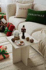 Elegant Christmas scene with a small table, nutcracker, snow globe, and festive cookies near a cozy sofa.