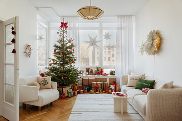 Stylish interior of Christmas arrangement with Christmass tree, white sofa and festive decorations and accessories.