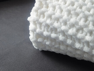 close up of a white soft knitted blanket edge on a dark gray matte background