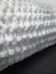 close up of a folded white soft chunky knitted blanket on a dark background