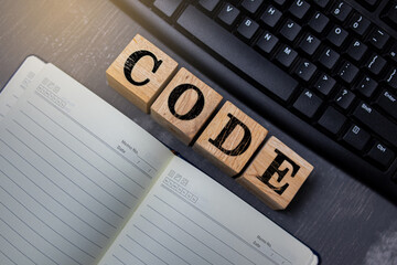 Wooden blocks with the word CODE placed on a keyboard and notebook background, symbolizing programming, software development, and modern digital technology concepts.