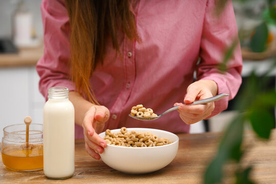 Woman female hands prepare a quick breakfast of dry round corn flakes balls, honey milk on a kitchen