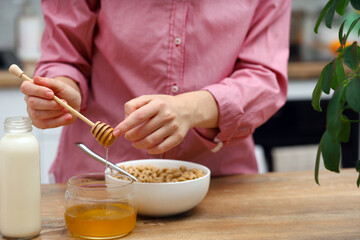 Woman female hands prepare a quick breakfast of dry round corn flakes balls, honey milk on a kitchen