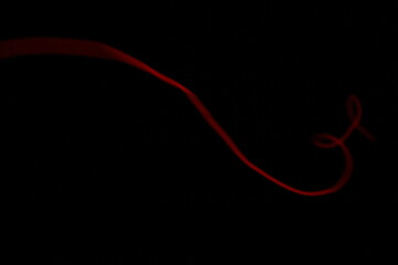 Abstract minimalist red glowing line creating a simple scribble and loop, isolated on a pure black background with copy space.