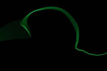 Abstract minimalist green glowing EL wire line, creating a smooth curve on a pure black background with copy space.