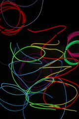 A chaotic, energetic scribble of multiple glowing EL wire lines in various colors, creating a vibrant abstract pattern on a black background.