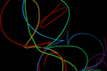 A chaotic, energetic scribble of multiple glowing EL wire lines in various colors, creating a vibrant abstract pattern on a black background.