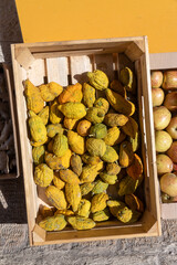 A wooden crate filled with yellow, knobby citrons (etrogim) lies next to a crate of apples, possibly at a local market stall.
