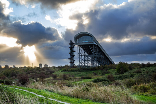 Silhouet of an indoor skiing slope building in a city park against a dramatic sky at sunrise