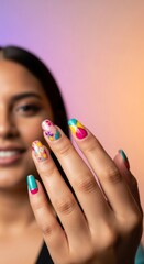 A smiling woman with wavy hair raises her hand to display vibrant multicolored nail polish designs against a soft pink background. Ideal for beauty, fashion, or nail art promotions in a clean close-up