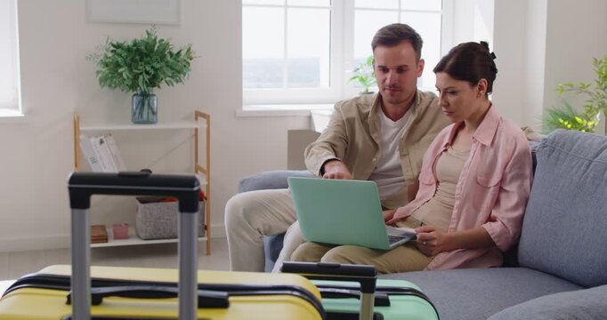Busy couple booking hotel and flight tickets online, woman holding credit card to pay for purchases at home. Young man and woman sitting on sofa with laptop together, paying for goods for travel