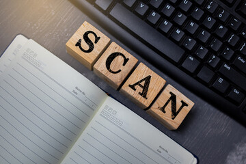 Wooden blocks spelling “SCAN” placed near a keyboard and notebook, representing digital scanning, data processing, and modern technology concepts in an organized workspace setting.
