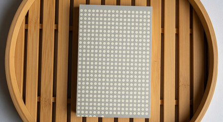 Dot Grid Notebook on Slatted Bamboo Tray: Clean Design Mockup.
An overhead, flat lay shot featuring a vertical notebook or journal with a sophisticated light gray cover patterned with small