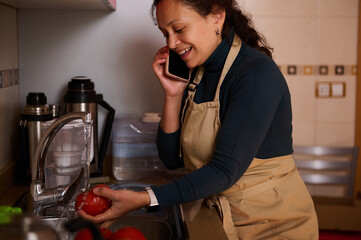 Busy Woman In Apron Washing Tomatoes At Kitchen Sink While Talking On Phone