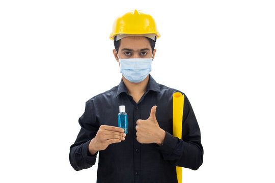 Engineer wearing face mask holding hand sanitizer and blueprints