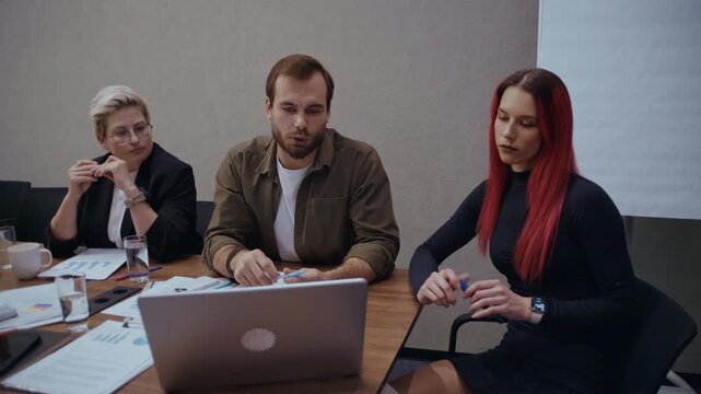 Colleagues in a modern office environment working together, analyzing business performance data on a laptop with documents scattered on the wooden table