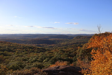 A panoramic view of a clear sunny day on top of a mountain surrounded by fall foliage.