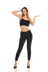 Full length studio shot of a tall brunette woman with long hair  smiling while posing with one hand on her head and the other holding an imaginary product on a white background