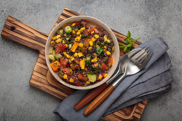 Quinoa salad with black quinoa, fresh tomatoes, corn, and cucumber representing healthy vegan and vegetarian food dark background