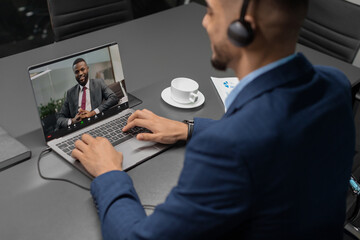 Middle eastern businessman participates in a video call with an african american CEO from a contemporary office. He focuses on his laptop while discussing business matters.