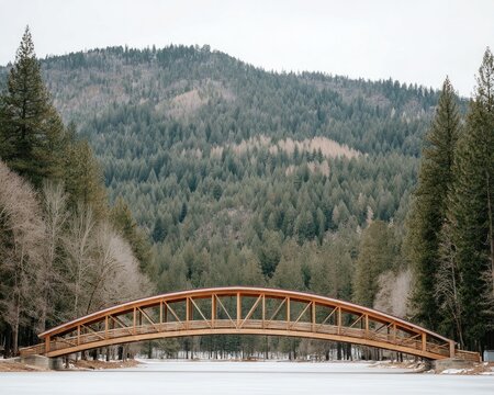 A wooden arch bridge spans an icy lake surrounded by green pines and snow-capped mountains in winter - Powered by Adobe