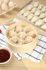 Steamed Dumplings in Bamboo Steamer with Soy Dipping Sauce and Fresh Ingredients on Wooden Table