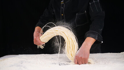 Professional chef making fresh handrolled noodles with flour dust on marble counter