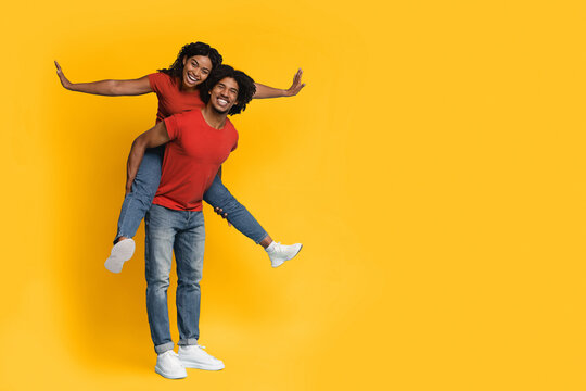 A couple shares a fun and happy moment with one partner giving a piggyback ride to the other. They are dressed in matching red shirts and are smiling joyfully, radiating energy. - Powered by Adobe