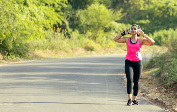 Happy Indian Woman Running Outdoors with Wireless Headphones and Smartwatch - Powered by Adobe