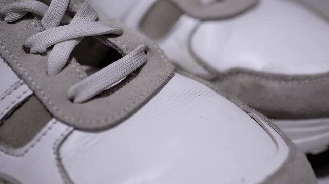 White sneakers with untied laces on a patterned surface. Grey suede accents add a touch of style. Perfect for lifestyle, fashion, and e-commerce visuals.