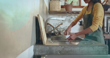 Washing woman in green apron rinsing white bowl at home concrete kitchen sink, with curved faucet