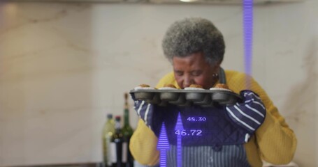 Inhaling senior woman holding metal muffin tray in kitchen, blue apron, showing purple overlay