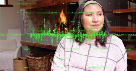 Sitting woman wearing light-knit grid sweater, headband, hoops by lit fireplace, green data overlay