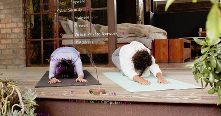 Practicing two women wearing workout wear bending into child pose on porch with mats, code overlay