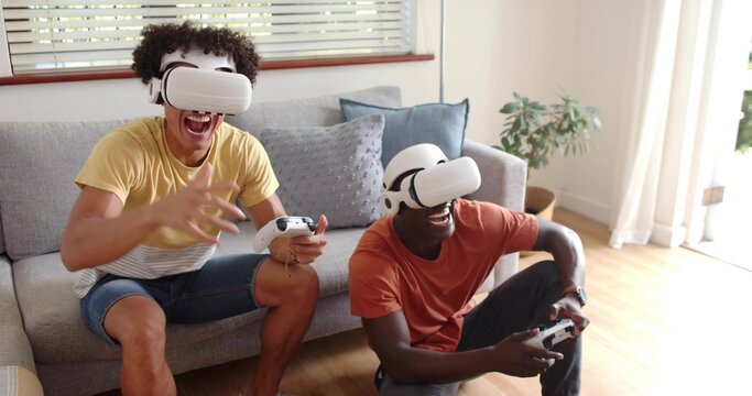 Playing friends wearing yellow and orange tees using white VR headsets and gamepads in living room - Powered by Adobe