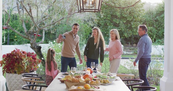 Smiling multigenerational family leaning for selfie on patio with smartphone, casual clothes, table - Powered by Adobe